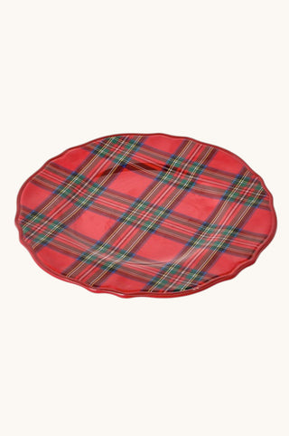 A round red plaid plate with a scalloped rim, featuring a tartan pattern in red, green, and yellow, set against a plain off-white background.