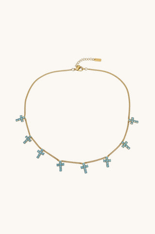 A gold chain necklace featuring multiple small cross charms embellished with light blue crystals, displayed on a clean off-white background.
