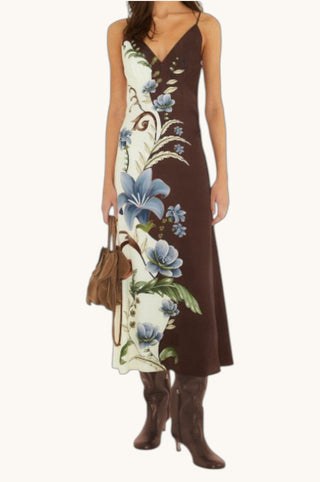A woman modeling a sleeveless brown midi dress with a cream side panel featuring a blue floral print, paired with brown knee-high boots and a brown handbag against a plain off-white background.