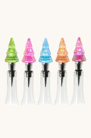 Five Christmas tree-shaped bottle stoppers in assorted colors (green, pink, blue, orange, and magenta) with clear glass bases, arranged in a row against a light cream background.