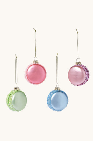 Four round Christmas ornaments hanging against a plain light background: two pink ornaments with textured edges and two pastel ornaments in mint green and light blue with glittery edges.
