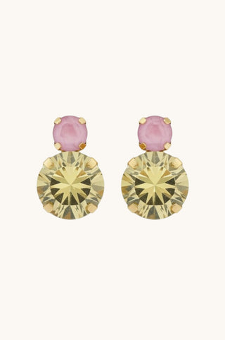 A pair of gold-toned drop earrings featuring a round faceted pale yellow crystal and a smaller oval pink crystal above it, set against a plain off-white background.