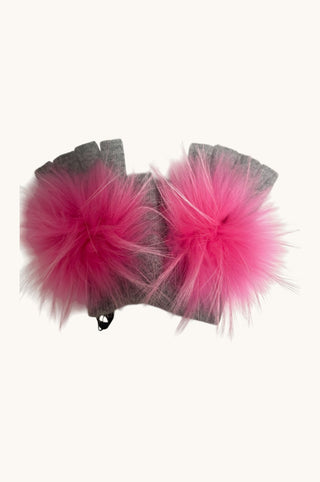 A pair of gray fingerless gloves with large, fluffy hot pink pompoms attached to the back of the hands, shown against a plain off-white background.