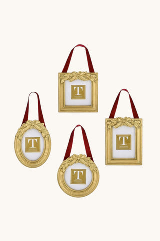 Four gold-framed hanging ornaments with red handles, each featuring a white insert with a gold monogram letter 'T', arranged on a light cream background.