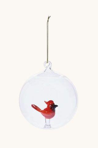 A clear glass hanging ornament shaped like a round bubble, containing a small red bird figurine with a black beak, suspended by a thin gold string against a plain off-white background.