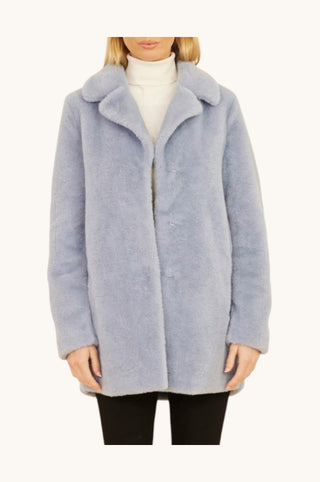 A model wearing a light blue fuzzy teddy coat over a white turtleneck sweater and black pants, shown from the neck down against a plain off-white background.