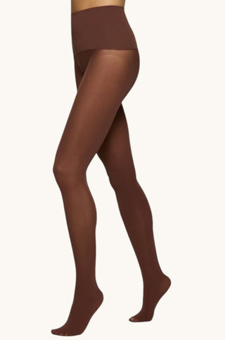A model's legs wearing sheer brown tights against a plain off-white background.